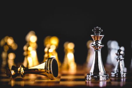 Closeup king chess piece defeated enemy or trade competitor by checkmate at end of chessboard game. Businessman moving chess to success competition by hand. Leadership and strategy managementの写真素材