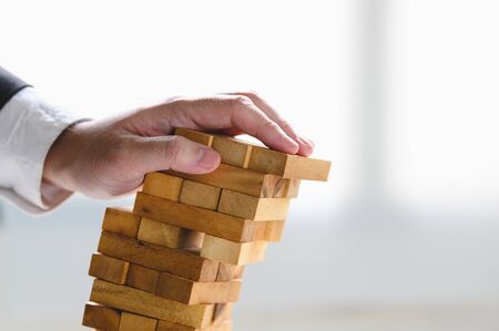Businessman collapsing stacked tower wood block by hand as failure or bankrupt project. Business organization and company unsuccessful progress. Strategy and money investment. Risk managementの写真素材