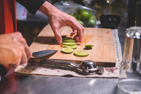 Closeup of professional bartender hand slicing lemon for making lemonade juice by knife in night club. Chef making drinks for guest in pub restaurant. Food and beverage concept.の写真素材