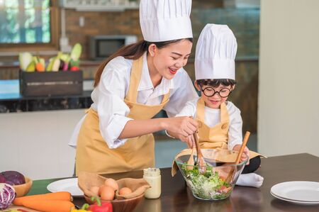 Happy beautiful Asian woman and cute little boy with eyeglasses prepare to cooking in kitchen at home. People lifestyles and Family. Homemade food and ingredients concept. Two Thai people lifeの写真素材