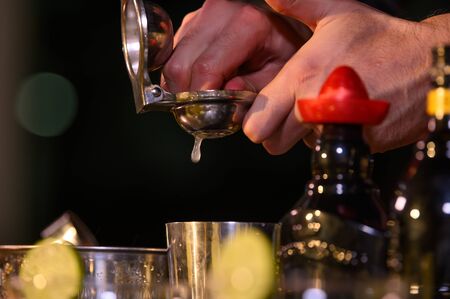 Closeup bartender hand preparing fresh juice cocktail in drinking wine glass with ice at night bar...