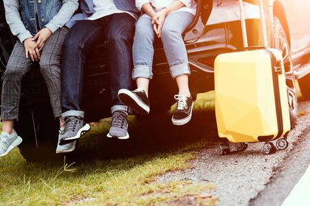 Closeup lower body of group of friends relaxing on SUV car trunk with trolly luggage along road trip with autumn mountain hill background. Freedom  road way. People lifestyle transportation travelの写真素材