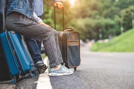 Closeup lower body of Asian couple relaxing on SUV car trunk with yellow trolly luggage along road trip with mountain hill background. Freedom road life. People lifestyle and transportation travelの写真素材