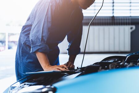 Car mechanic holding clipboard and checking to maintenance vehicle by customer claim order in auto repair shop garage. Engine repair service. People occupation and business job. Automobile technicianの写真素材