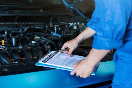 Car mechanic holding clipboard and checking to maintenance vehicle by customer claim order in auto repair shop garage. Engine repair service. People occupation and business job. Automobile technicianの写真素材