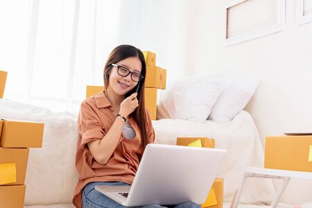 Beauty Asian woman using laptop and calling phone on bed. Business and Technology concept. Delivery and Online shopping concept. Post and Service theme. People lifestyle remote work in domestic houseの写真素材
