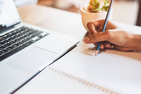 Close up of working woman hand using laptop computer and writing letter on notebook paper in office desk. Business and people lifestyles. Financial and Economy investment. Work from home conceptの写真素材