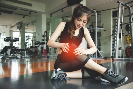 Asian woman injuries during workout at knee in fitness gym sport center. Medical and Healthcare concept. Exercise and Training theme. People healthy lifestyle and leisure activity problemの写真素材