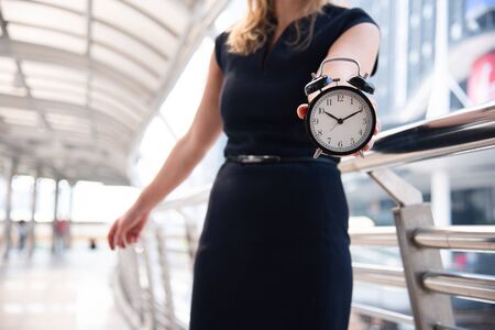 Business women show alarm clock and shocked with late in rush hours when going to work in city urban...