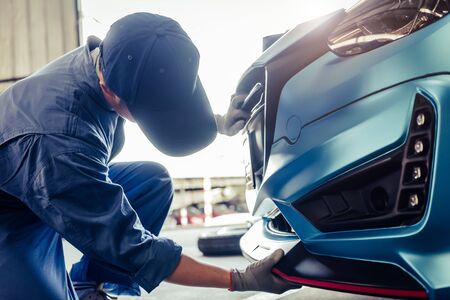 Mechanics installing front skirt at auto repair shop garage. Transportation and Business concept. Automobile technician maintenance vehicle by customer claim order. Car salon accessories decorationの写真素材