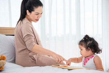 Asian mother teaching girls daughter to reading books in house. Quarantine in home concept. Happy family theme.の写真素材