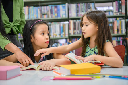 Two cute girls conflict while reading books in library when teacher teaching. People lifestyles and education. Young friendship and Kids relationship in school concept. Daycare themeの写真素材