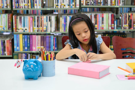 Asian girl folding and crafting paper in library during art class. Education and activity conceptの写真素材