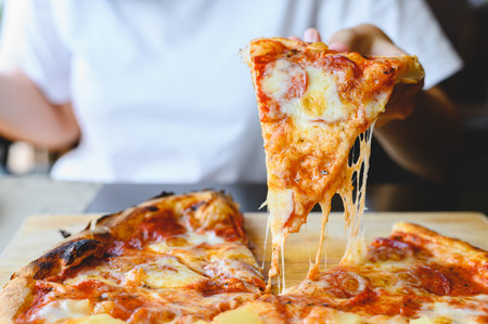 Wood fire cheesy pizza slice in hand. Traditional Hawaiian and Salami pizza savory dish flavour of origin Italian restaurant. Wood-Fired Oven Pizza with people holding pizza backgroundの写真素材