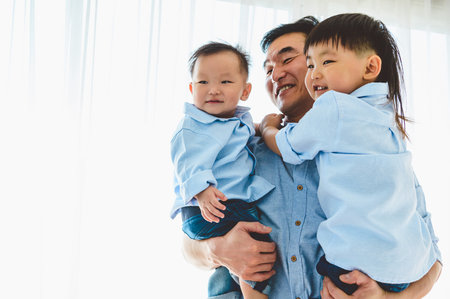 Happy father carrying two children in bedroom at their house. Family living and having positive...
