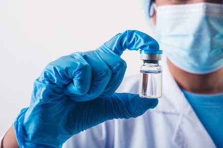 Closeup vial of covid-19 vaccine in hand of professional scientist or doctor in laboratory for treatment with mask gloves and lab coat on white background. Health business and industry concept.の写真素材
