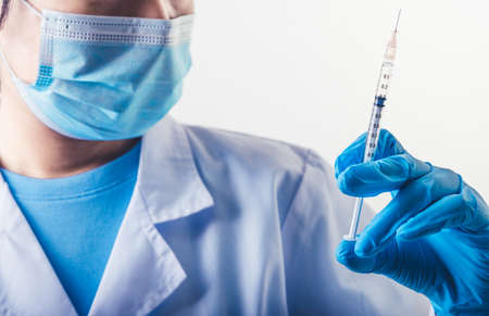 Closeup needle of covid-19 vaccine in hand of professional scientist or doctor in laboratory for treatment with mask gloves and lab coat on white background. Health business and industry concept.の写真素材