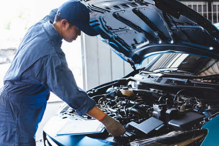 Car mechanic checking to maintenance vehicle by customer claim order in auto repair shop garage by list in clipboard. Engine repair service. People occupation and business job. Automobile technicianの写真素材