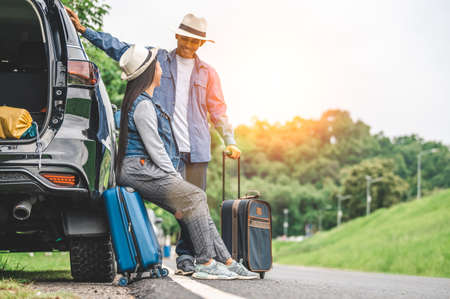 Closeup lower body of Asian couple relaxing on SUV car trunk with yellow trolly luggage along road trip with mountain hill background. Freedom road life. People lifestyle and transportation travelの写真素材