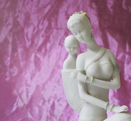 White ceramic figurine of mother and child with pink backdrop.の写真素材