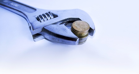 Adjustable wrench gripping a stack of coins with shallow depth of field.の写真素材
