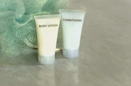 Two tubes of body lotion and body conditioner with a loofah on bathroom tile tabletop.の写真素材