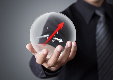 Businessman holds crystal ball with rising red graph and broken white graphの写真素材