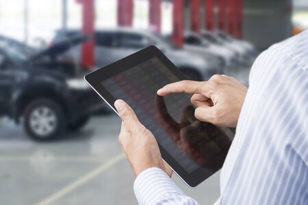 Closeup of a man checking the car on touchscreen tablet in a garageの写真素材