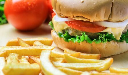 Burger on wooden plate with french fries and vegetablesの写真素材