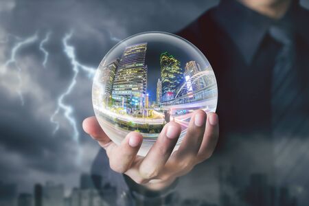 businessman hand hold crystal ball with city night inside with storm and   lightning backgroundの写真素材