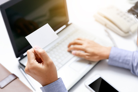 businessman hold blank paper card on hand with office desk backgroundの写真素材