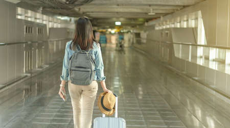 Asian woman walk with luggage and backpack at the airport terminal walkwayの写真素材