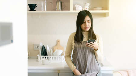 Young Asia woman use mobile phone in kitchen pantry at homeの写真素材