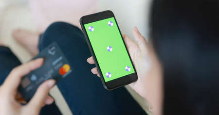 Woman sitting on sofa and Using Smart phone and credit card for online shoppingの写真素材