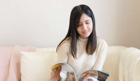 Young Asia woman reading book on sofa at homeの写真素材