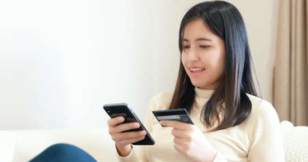 Woman sitting on sofa and Using Smart phone and credit card for online shoppingの写真素材