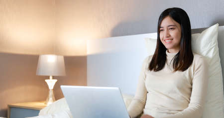 Asian woman sitting and working on laptop computer on bedの写真素材