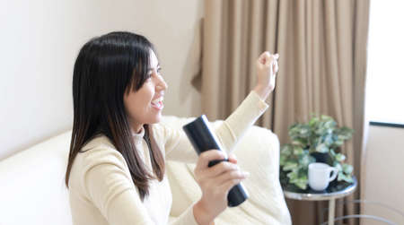 young Asian woman sitting on sofa and watching television at homeの写真素材