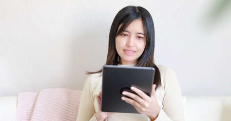 Asian woman use digital tablet and sit on sofa at homeの写真素材
