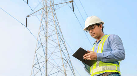 Electrical Engineer Working On Digital Tablet With Electric Power Pole Backgroundの写真素材