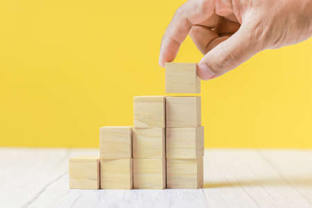 Hand arranging wooden block stacking as step stair on yellow background. Business growth concept.の写真素材