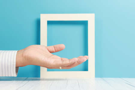 Hand holding blank photo frame on blue wall background with copy space.の写真素材