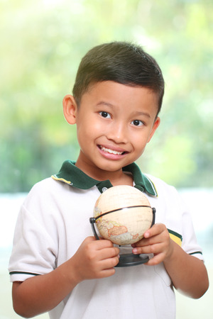 Little boy is holding a globe on green backgroundの写真素材