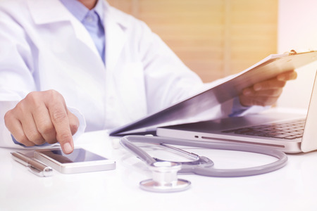 Woman doctor using mobile smart phone and reading diary at office deskの写真素材