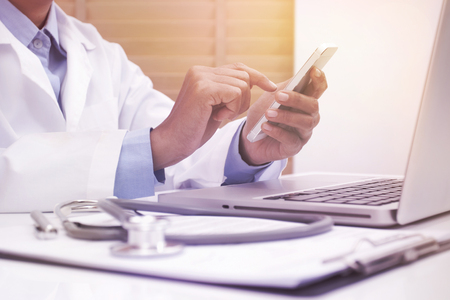 Woman doctor using mobile smart phone and laptop computer at office deskの写真素材