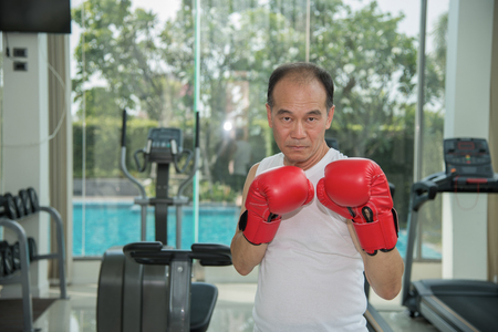 Old man wearing red boxing gloves exercising in fitness look to camera, look to camera ready to fighting, copy space for textの写真素材