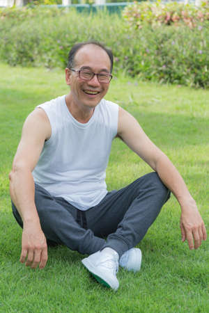 Asian old man smile and sit on the grass at the park. Happiness, relaxing.の写真素材