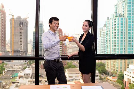 businessman and businesswoman are drinking champagne talking and smiling while celebrating in office, successful business concept.の写真素材