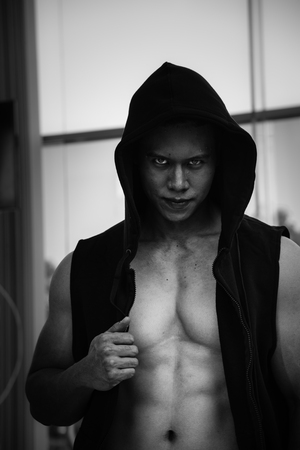 horror muscular man wear black jacket with hood standing behind the window, black and white picture, dangerious man conceptの写真素材