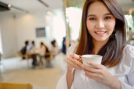 Portrait of beautiful face woman and holding a cup of coffee in her hand in blur background coffee shop, she drink coffee in the morningの写真素材